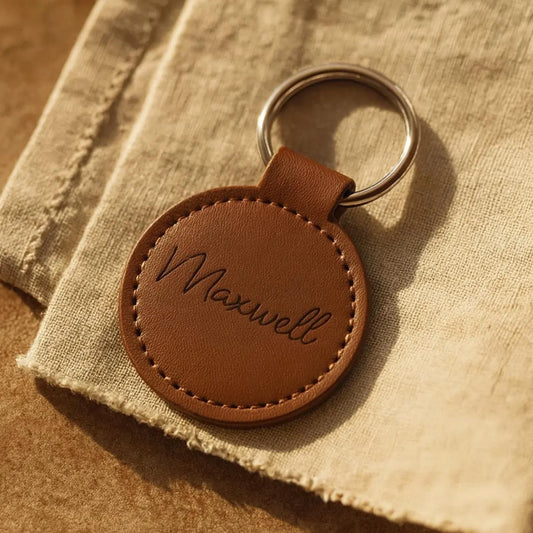 Brown leather keychain with 'Maxwell' engraving on a textured fabric background